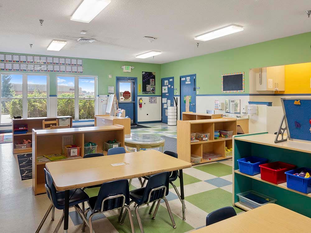 Empty colorful classroom with tables, chairs, and shelves of toys