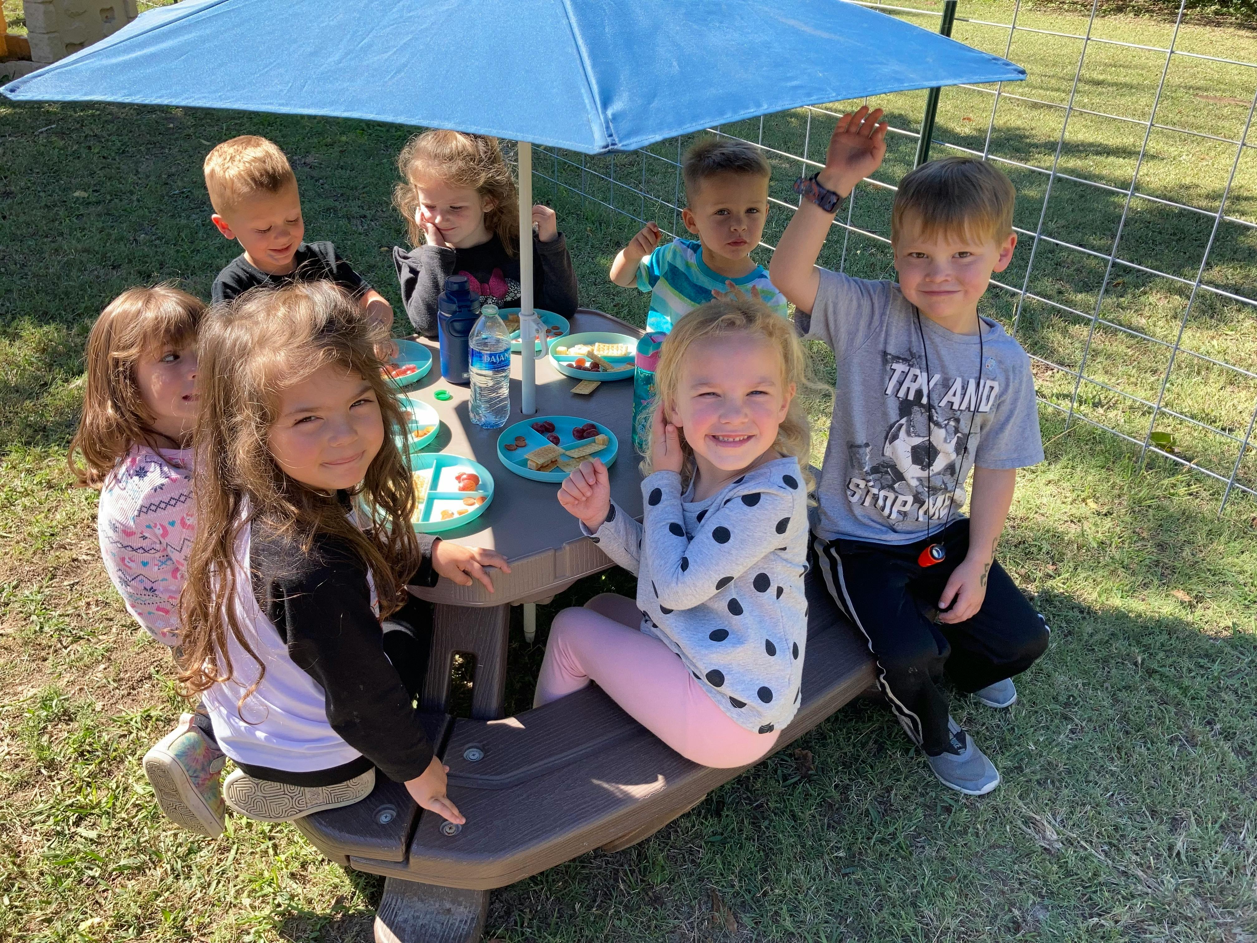 Group of children sitting at a picnic table under an umbrella