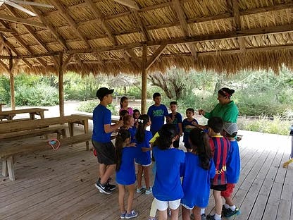 Adults and children gathered under a thatched roof structure