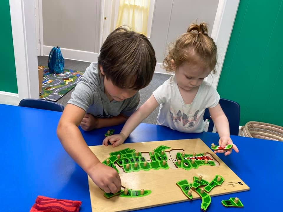 Two children playing with a puzzle on a blue table