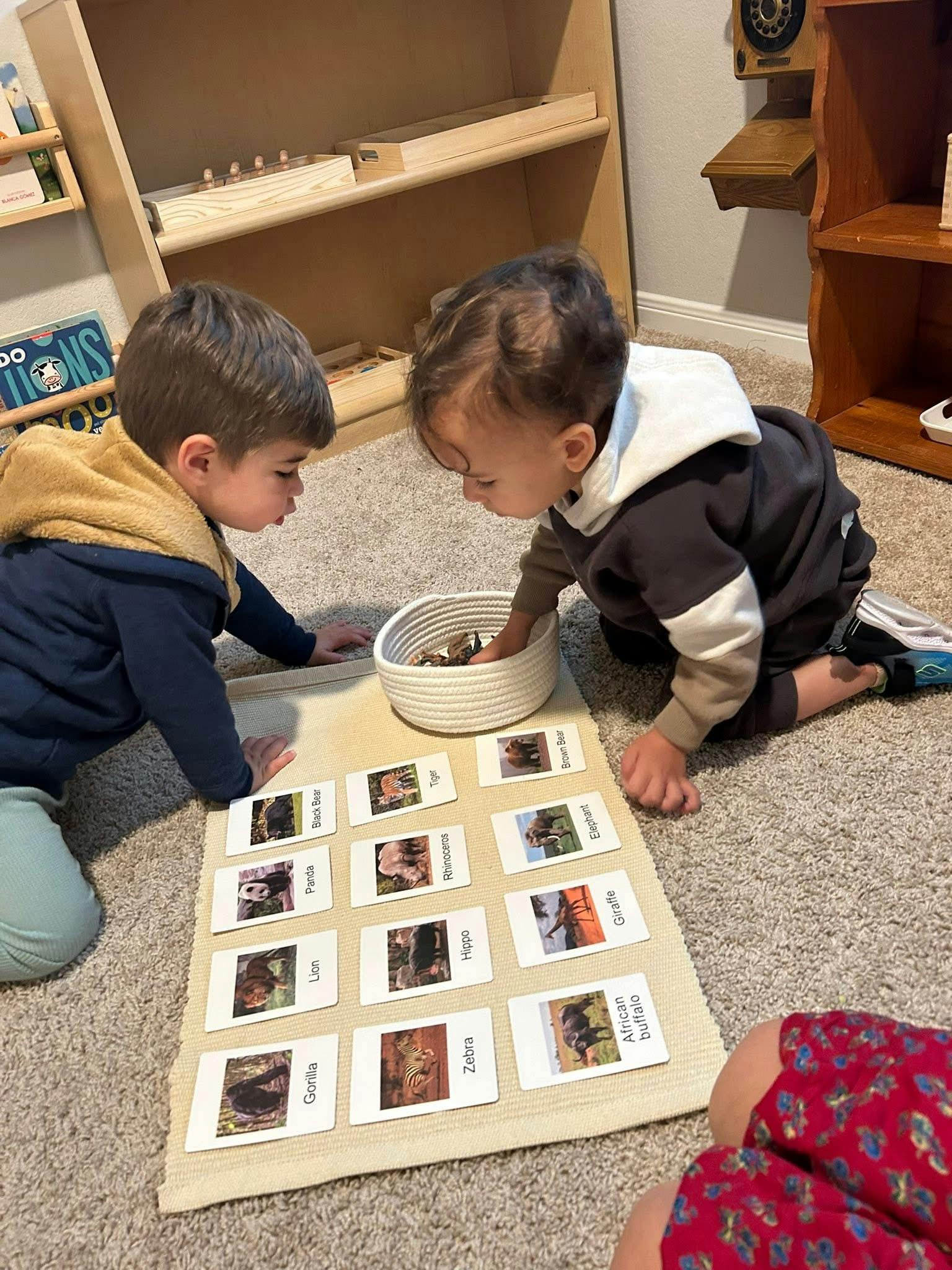 Two children on the floor playing with animal picture cards and a basket