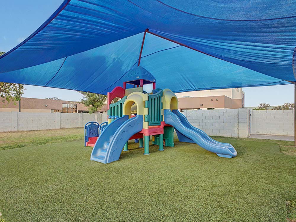 playground with slides on artificial turf under a blue shade covering
