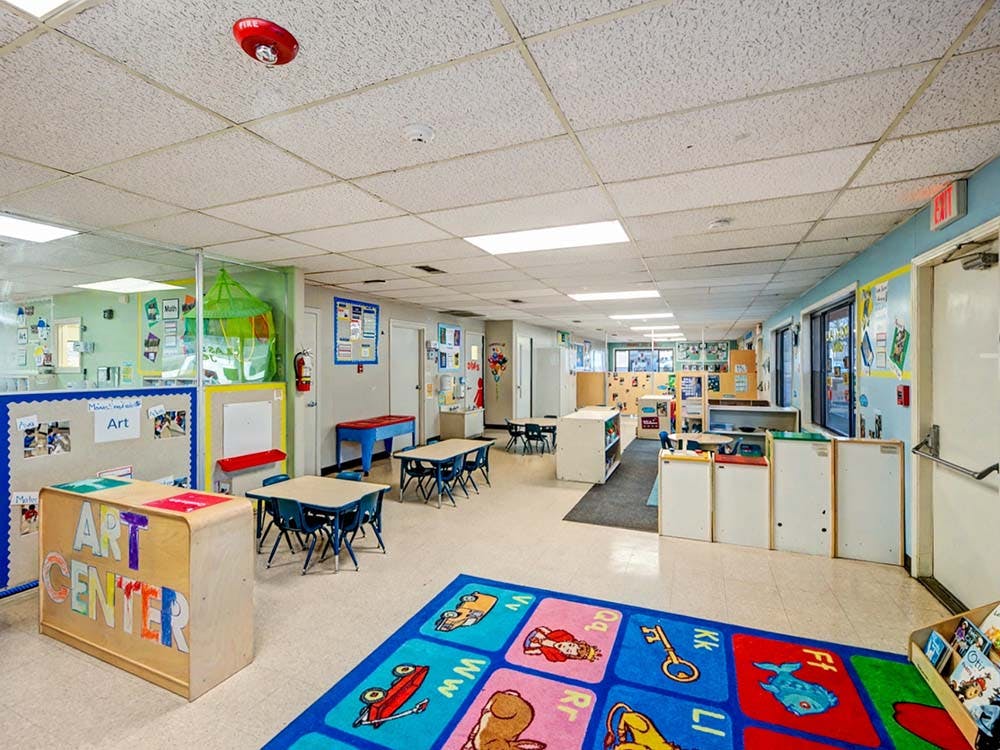 A colorful kindergarten classroom with small tables and chairs, and an "Art Center" sign