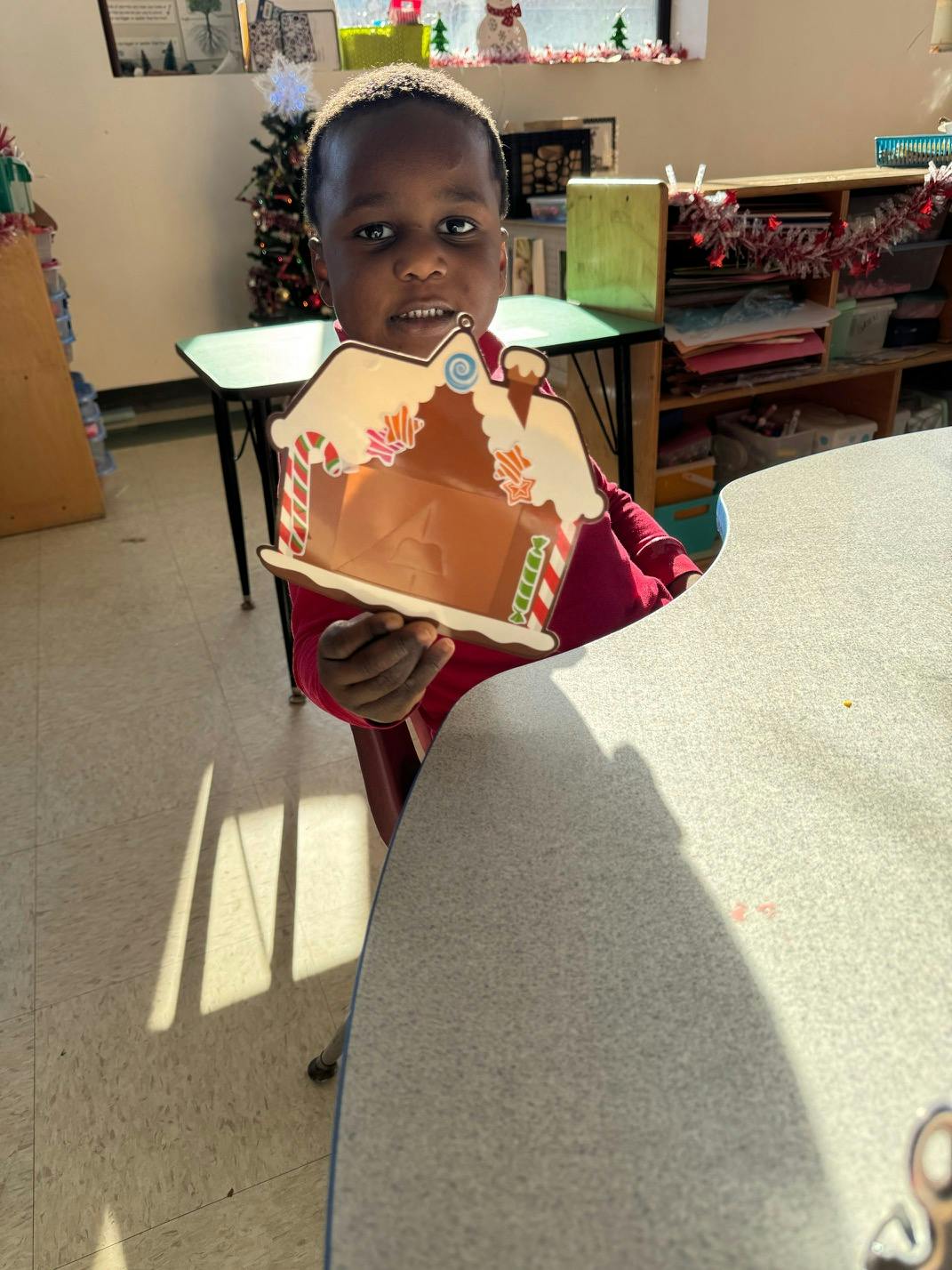 Child holding up a gingerbread house craft in a classroom
