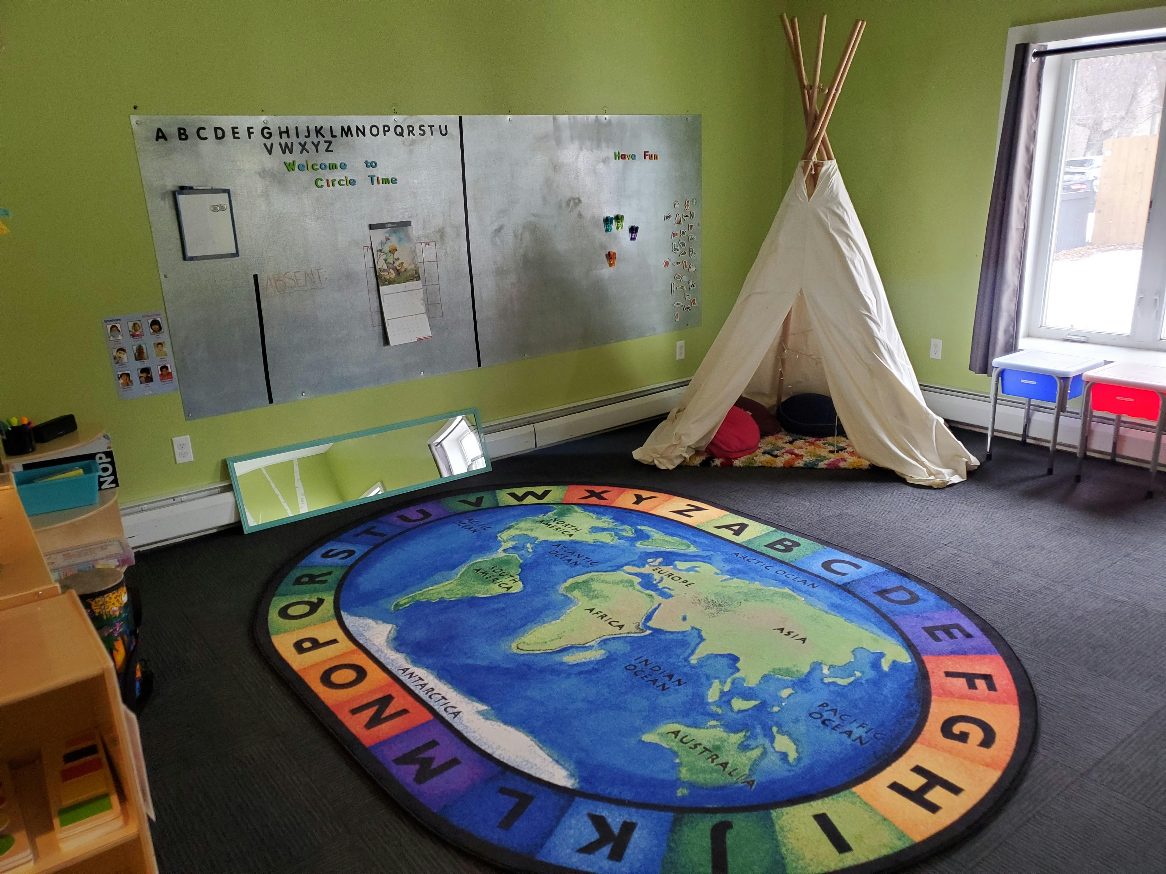 Classroom with a world map rug, a teepee, and a whiteboard