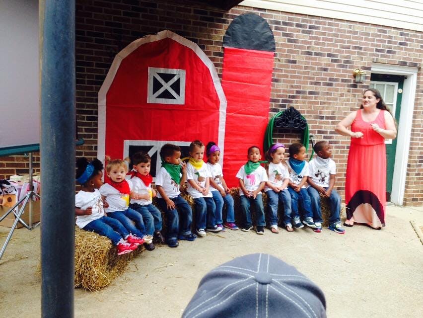Adult speaking to a group of children sitting on a hay bale and ground
