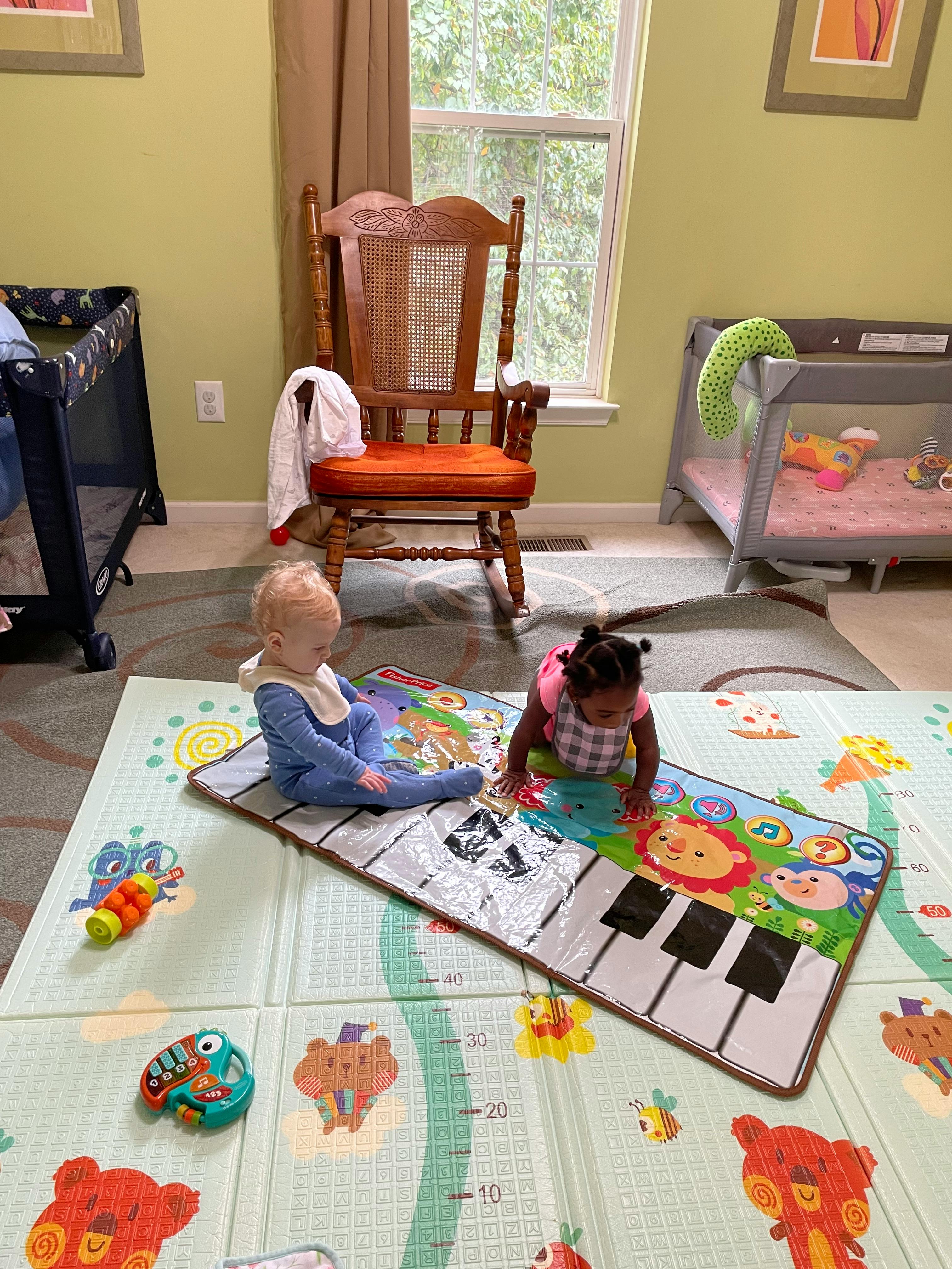 Two children playing on a colorful mat in a room with cribs