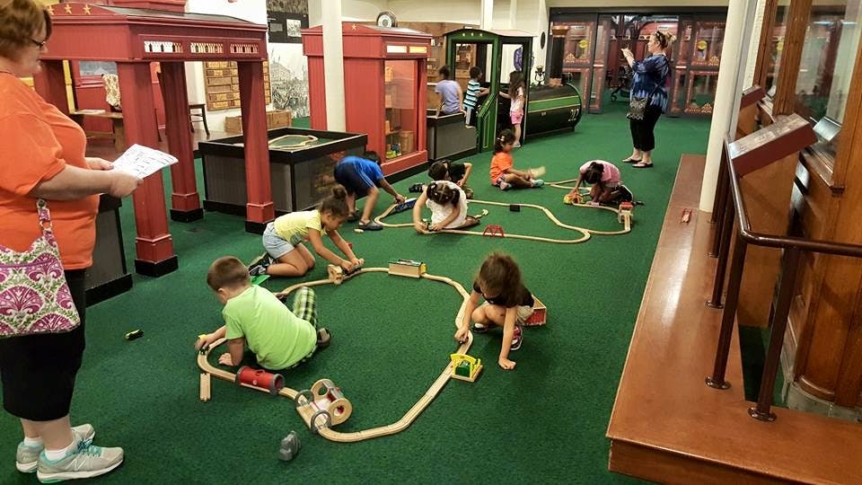 Children playing with toy trains on a green carpeted floor