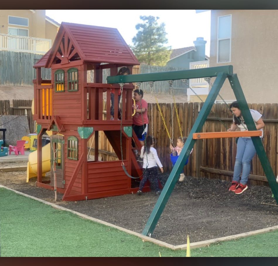 People and children playing on a backyard playset with swings and a playhouse