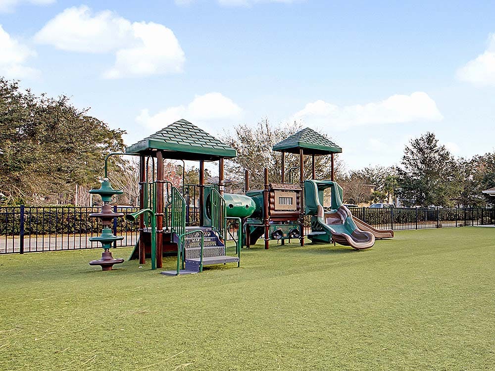 A playground with green turf and a black fence