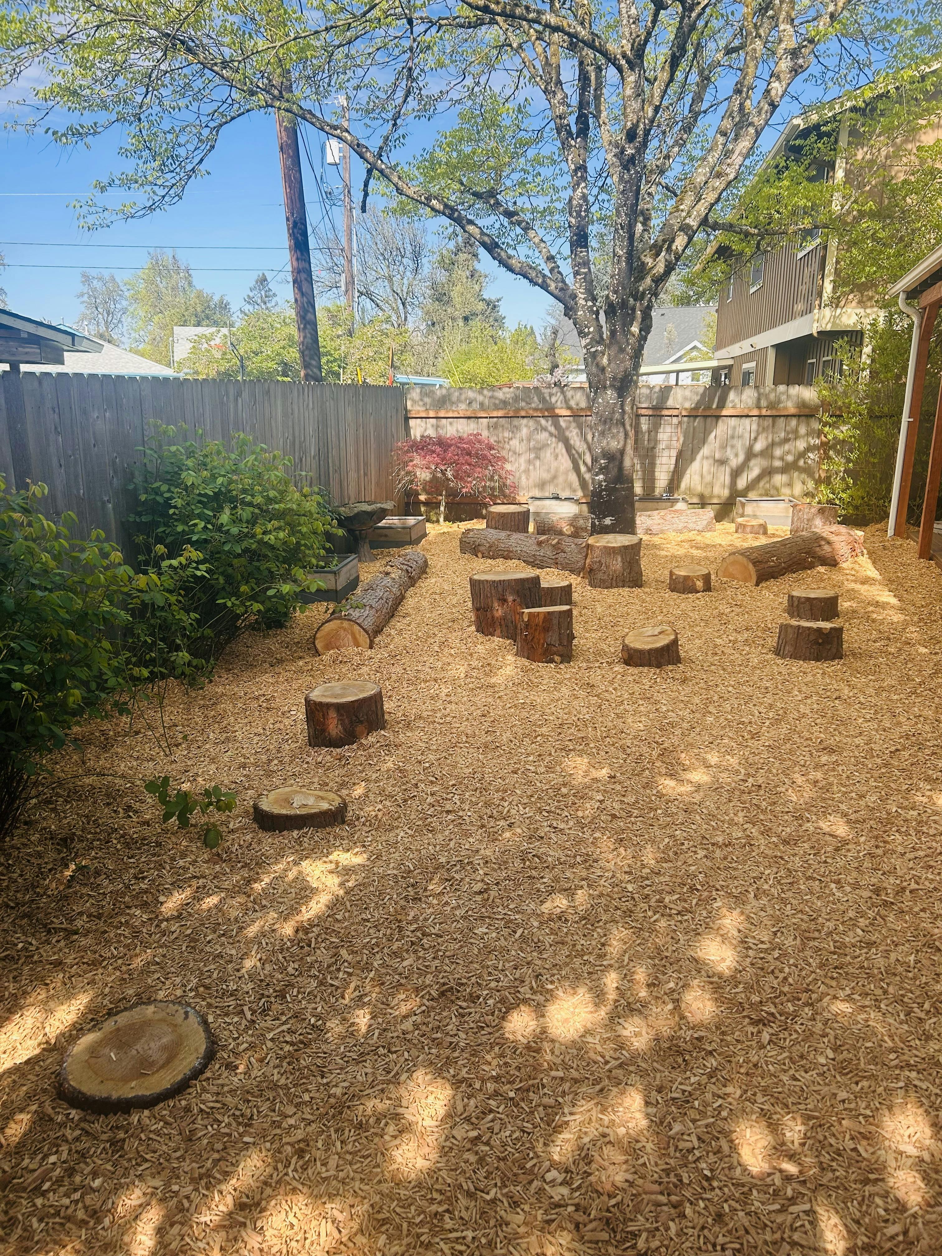 Outdoor natural play area with wood chips, log stumps, and log benches