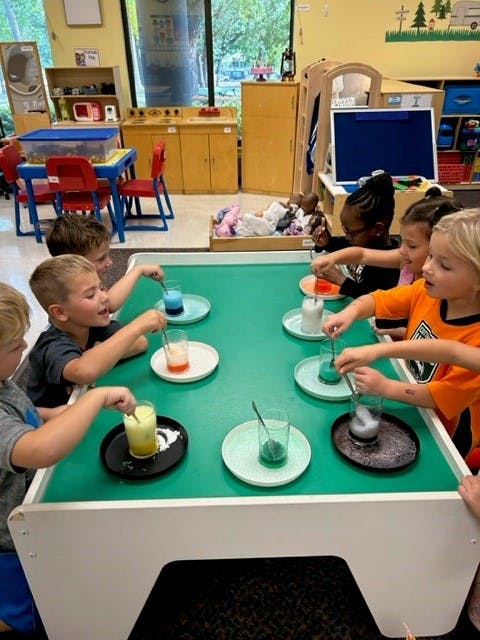 Children sitting at a table conducting a science experiment with colored liquids