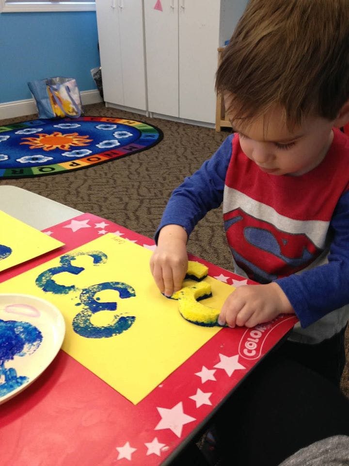 Child stamping blue paint onto yellow paper with a number three sponge