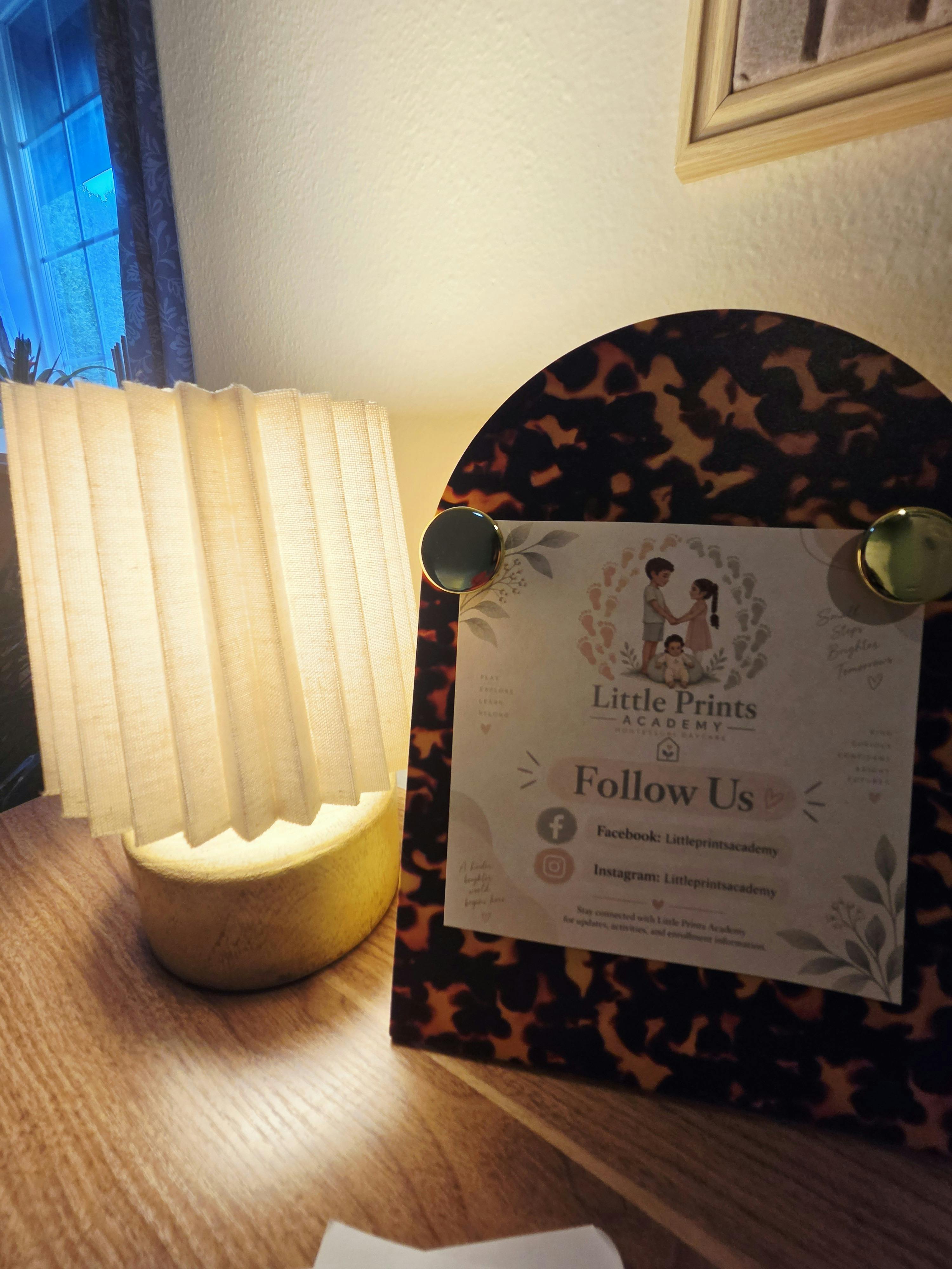 Sign for Little Prints Academy daycare displayed next to a small table lamp