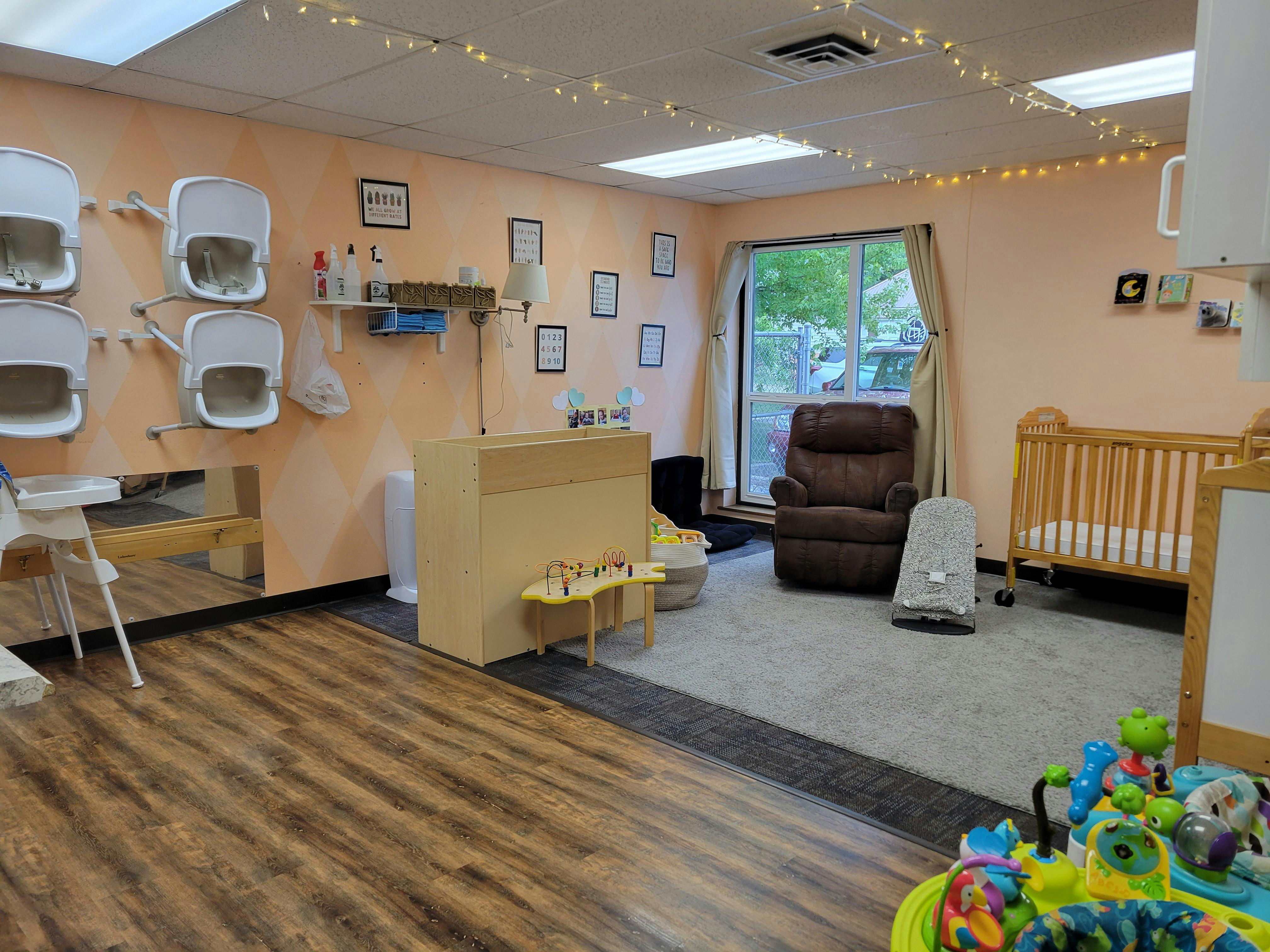 A childcare room with wall-mounted high chairs, a changing table, a recliner, and a crib