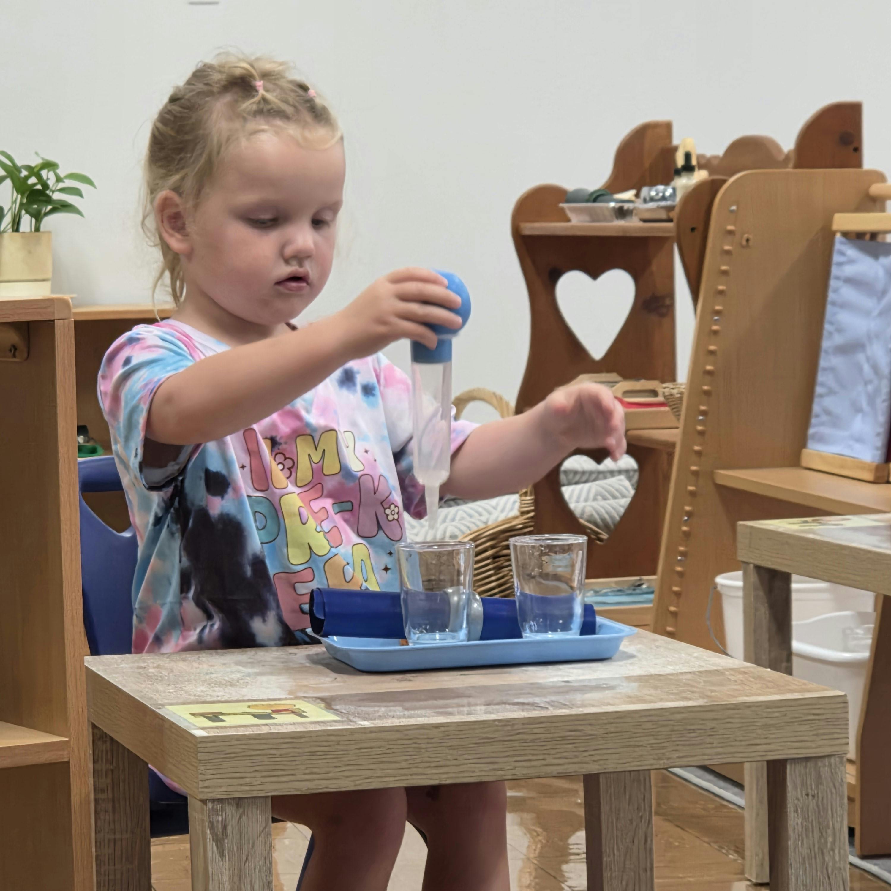 Child using a dropper to transfer liquid between two glasses