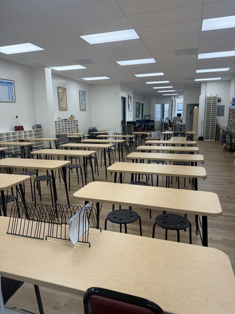 Empty classroom with light-colored desks and black stools arranged in rows