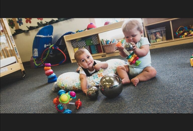 Two babies playing with toys on the floor