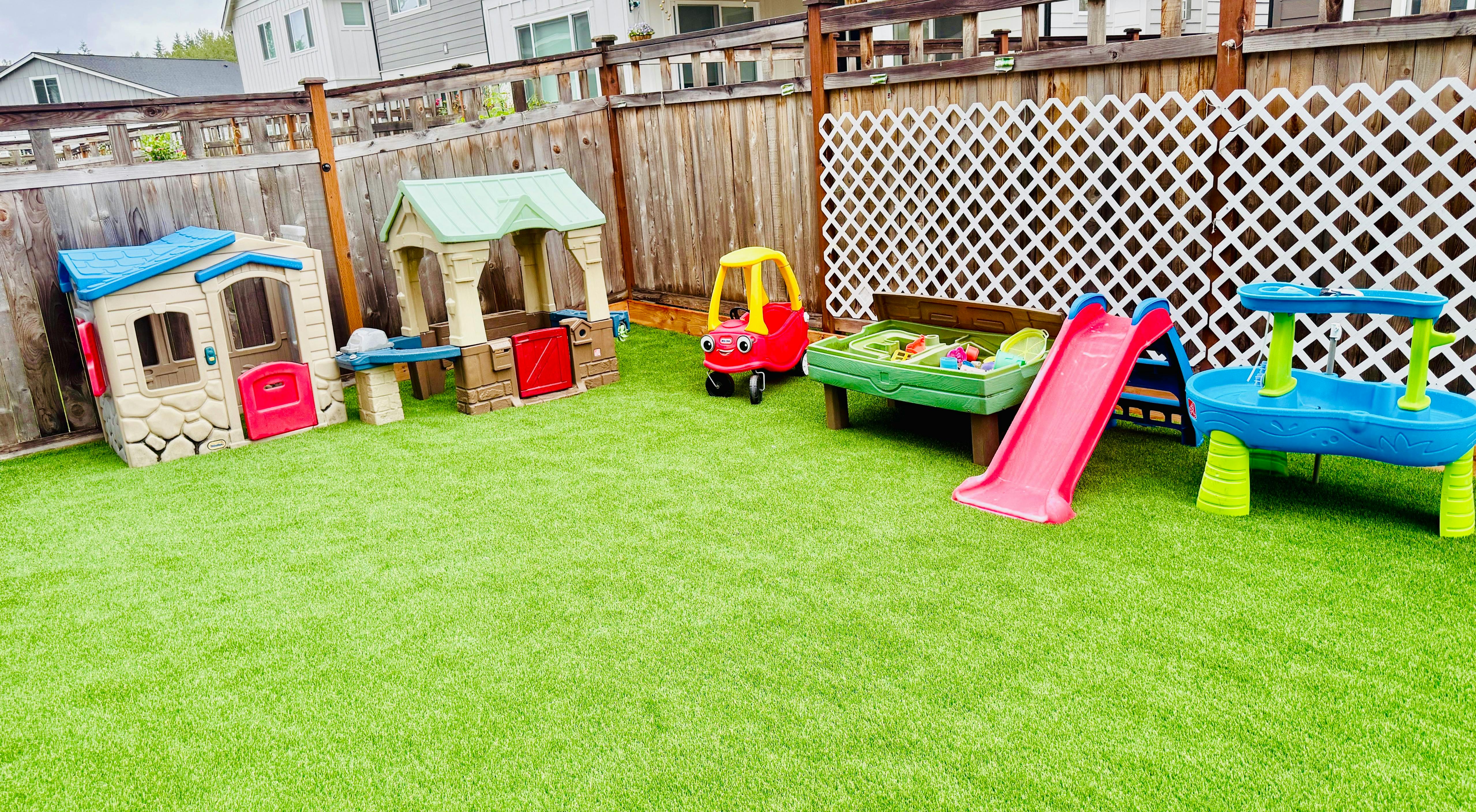 Play area with toy houses, car, slide, and water table on artificial grass