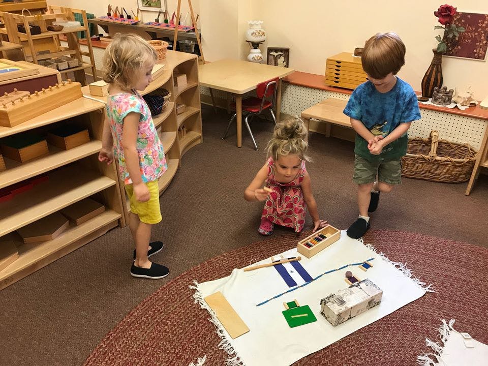 Three children playing with learning materials on a rug
