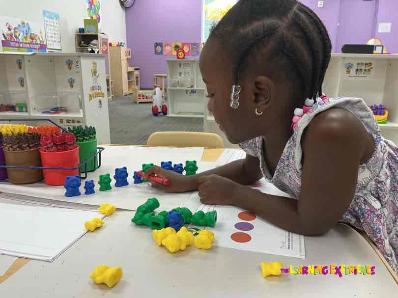 Child playing with bear counters at a table in a classroom