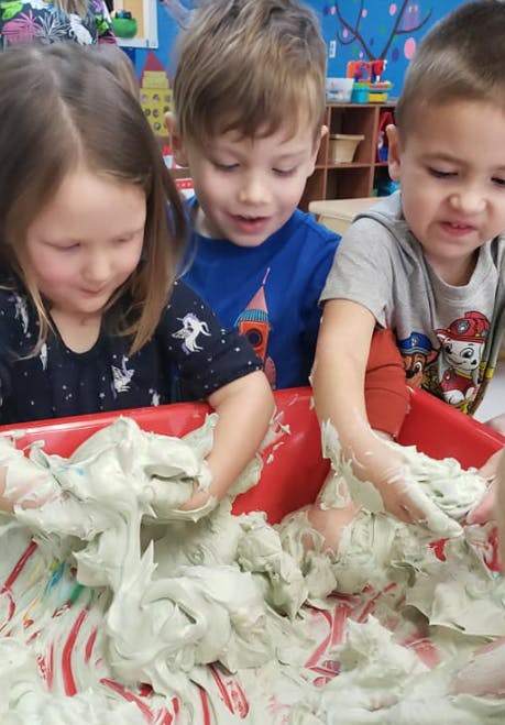 Three children playing with a sensory bin filled with a light-colored, gooey substance