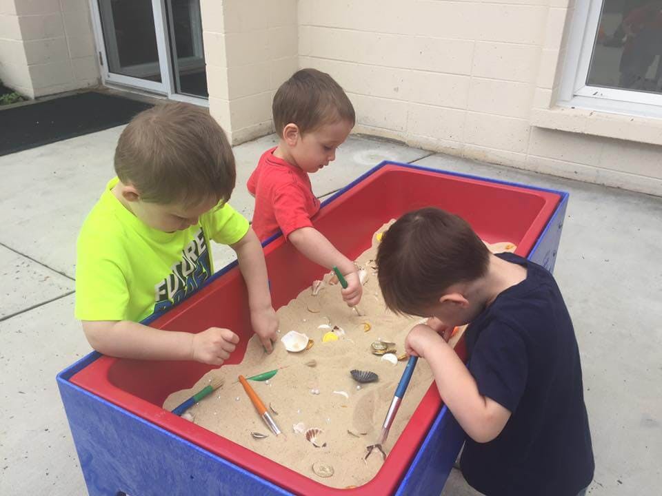 Three children playing in a sand table