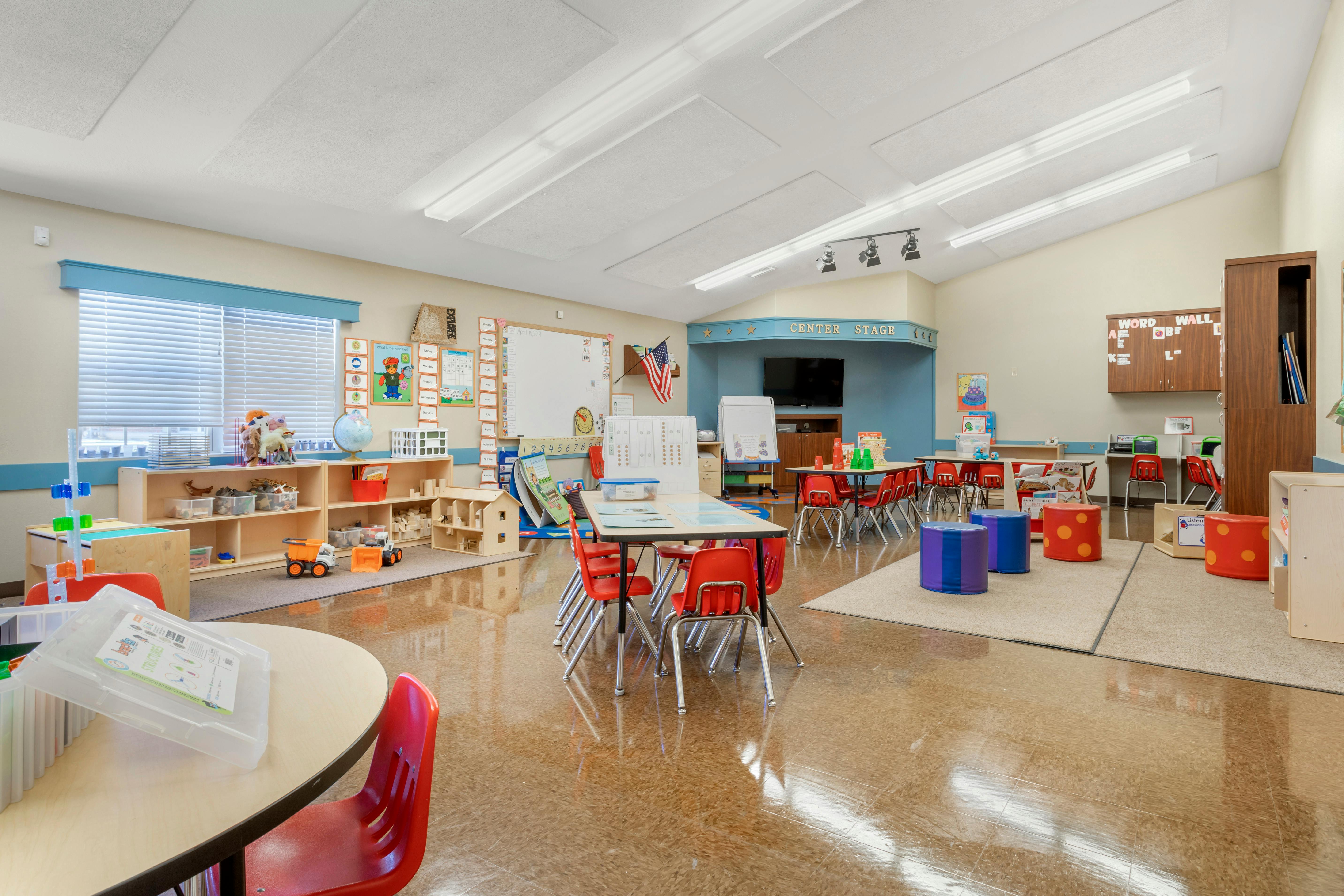An empty early childhood classroom with small tables and chairs