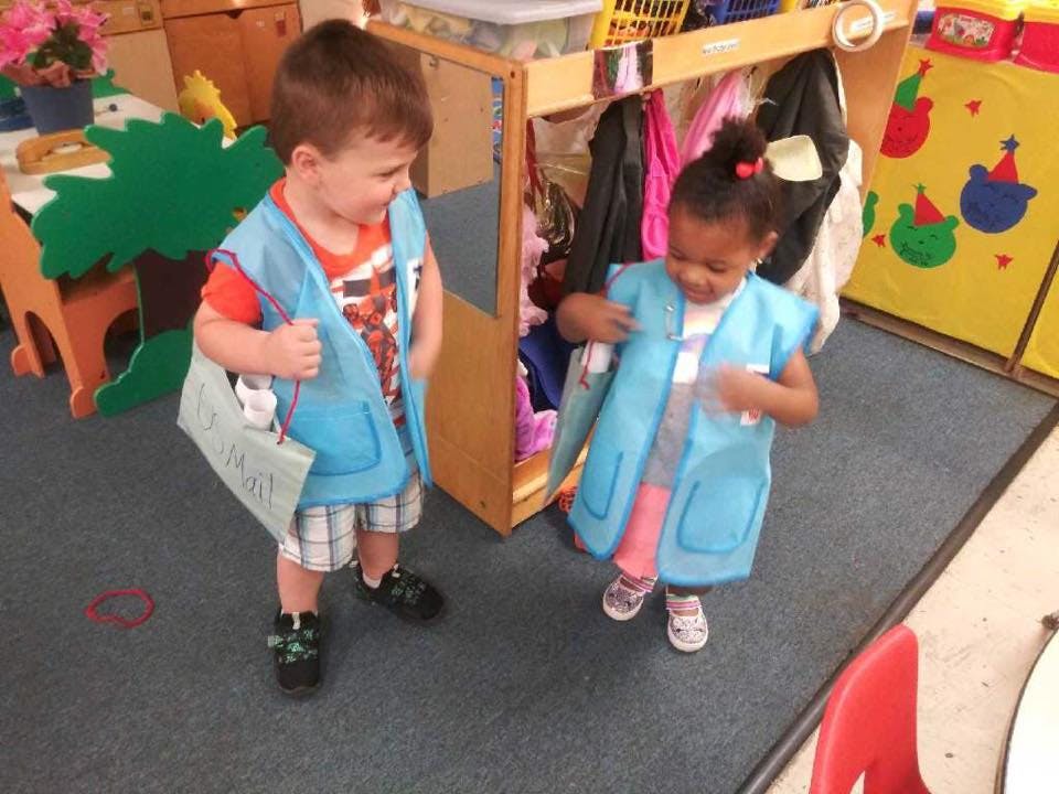 Two children wearing blue vests in a classroom