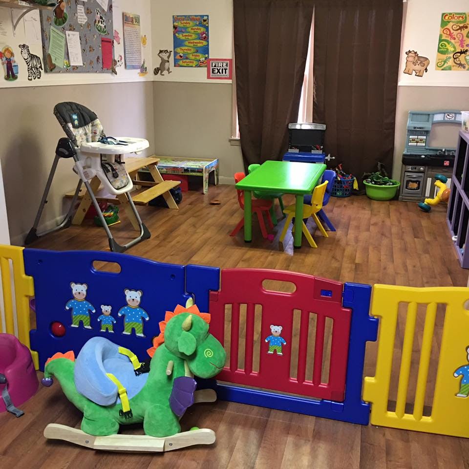 Playroom with a green rocking dinosaur, playpen, high chair, and small tables
