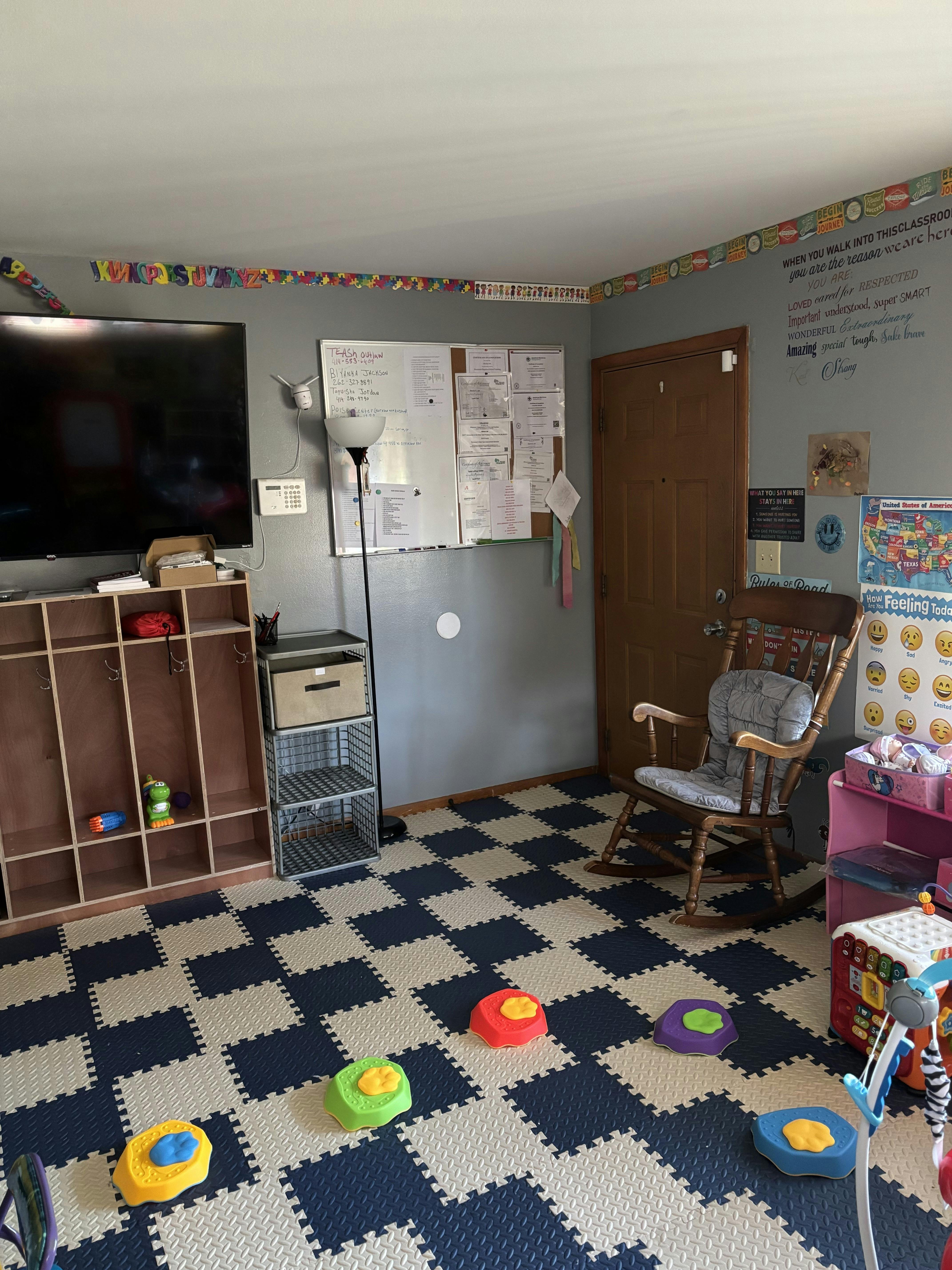 Classroom with checkered floor mats, cubbies, a rocking chair, and wall decorations