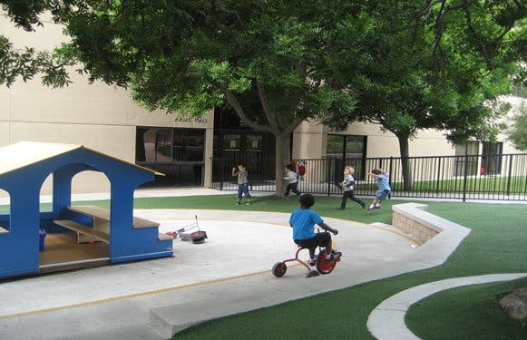 Child on a tricycle on a playground with other children playing