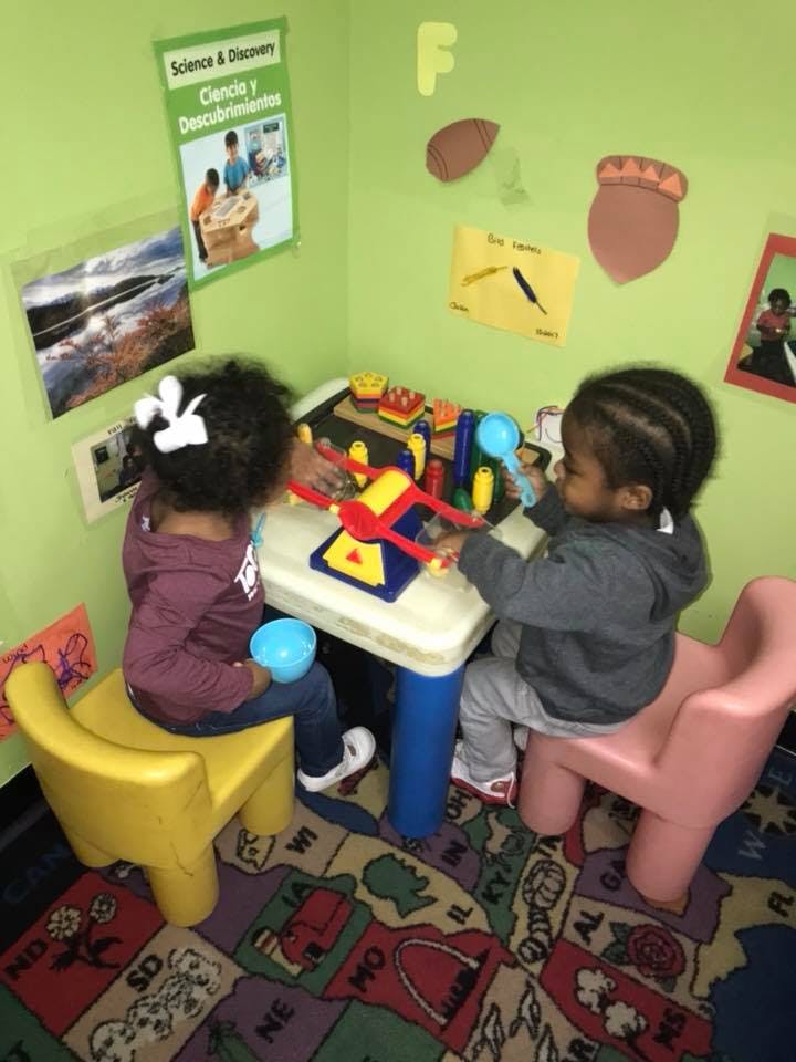 Two children playing with toys at a small table in a classroom