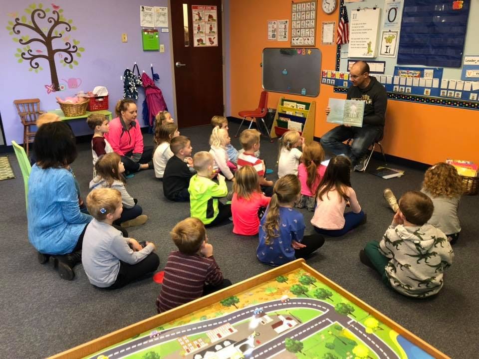 Adult reading a book to a group of children in a classroom