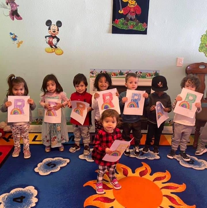 Group of children holding up papers with the letter R and a rainbow