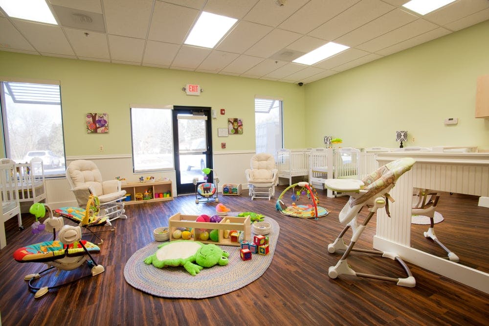 Infant and toddler room with cribs, play mats, and high chairs