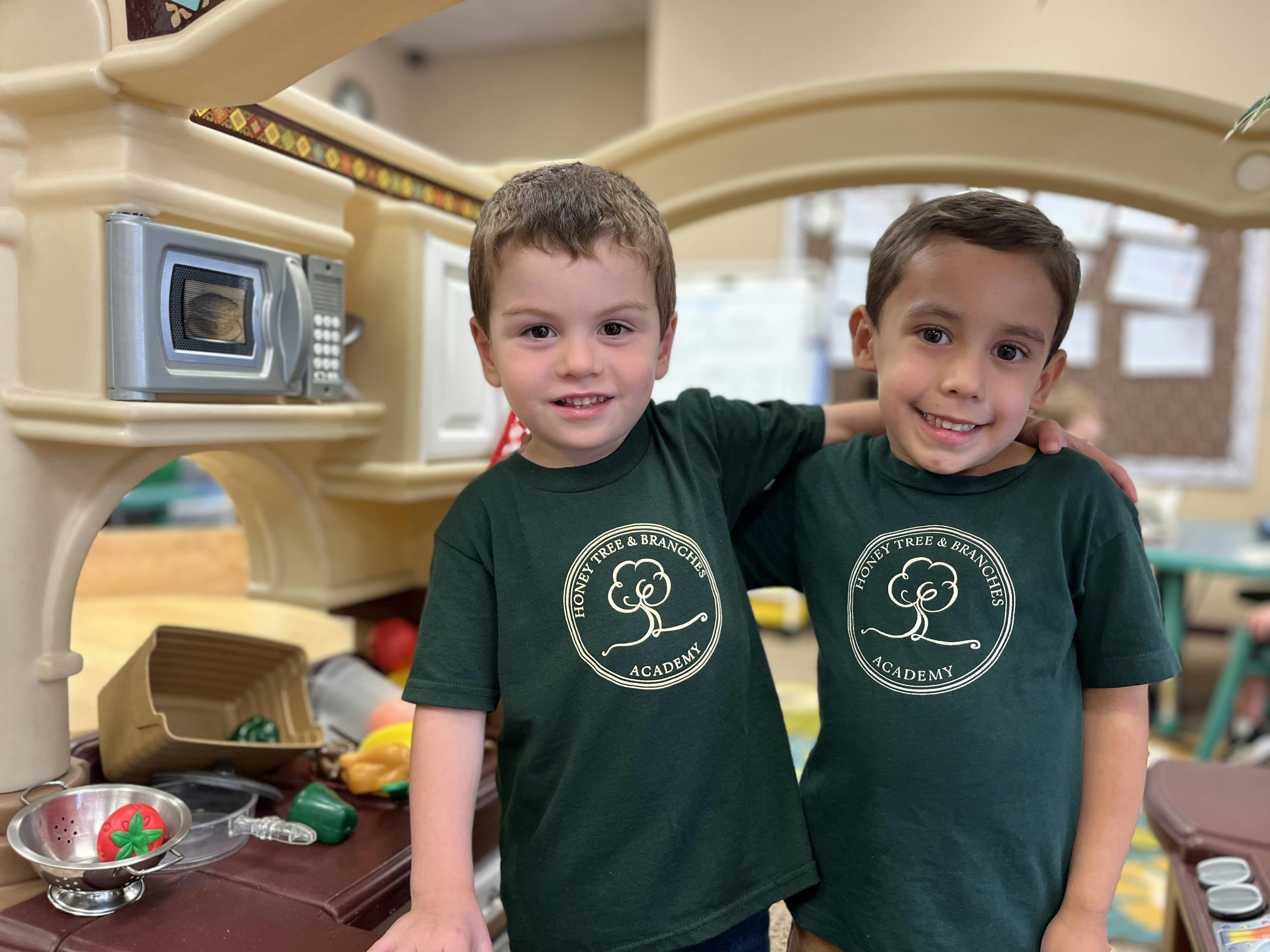 Two children in matching shirts standing together in a play kitchen