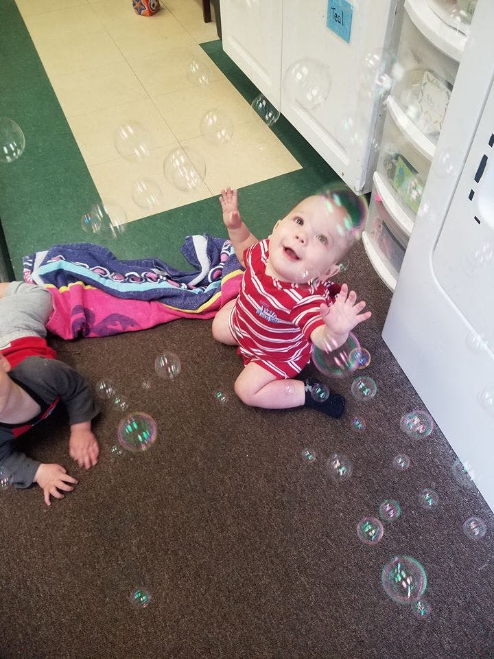 Child in red and white striped outfit reaching for bubbles on the floor