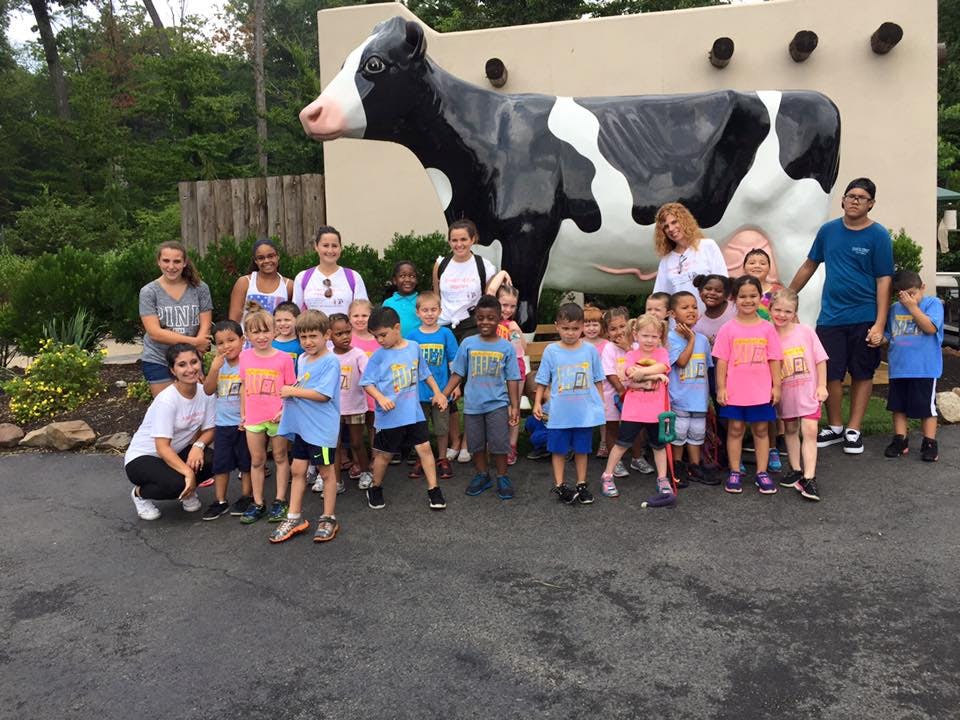 Group of adults and children posing in front of a large cow sculpture