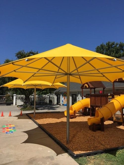 Yellow umbrellas providing shade over a playground with slides