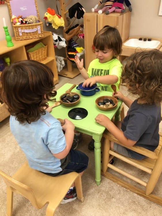Three children playing with bowls and small objects at a green table
