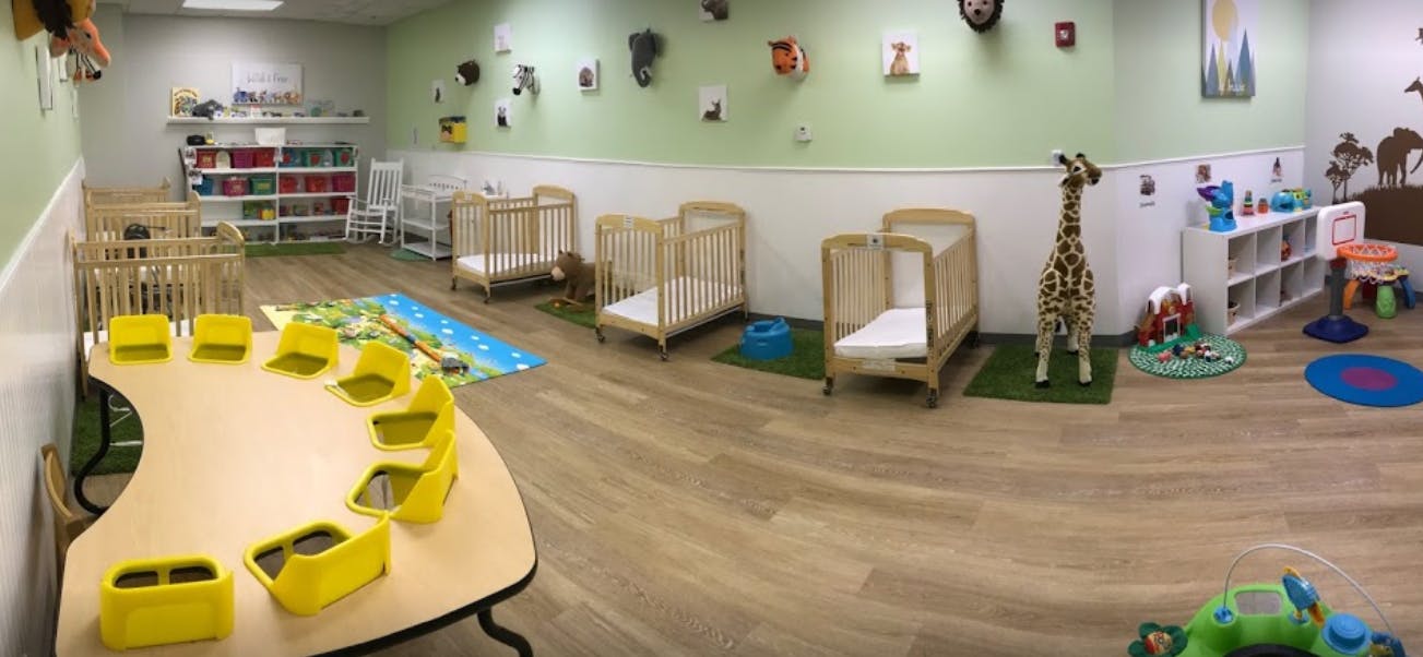 Daycare room with cribs, small table with yellow chairs, and toys