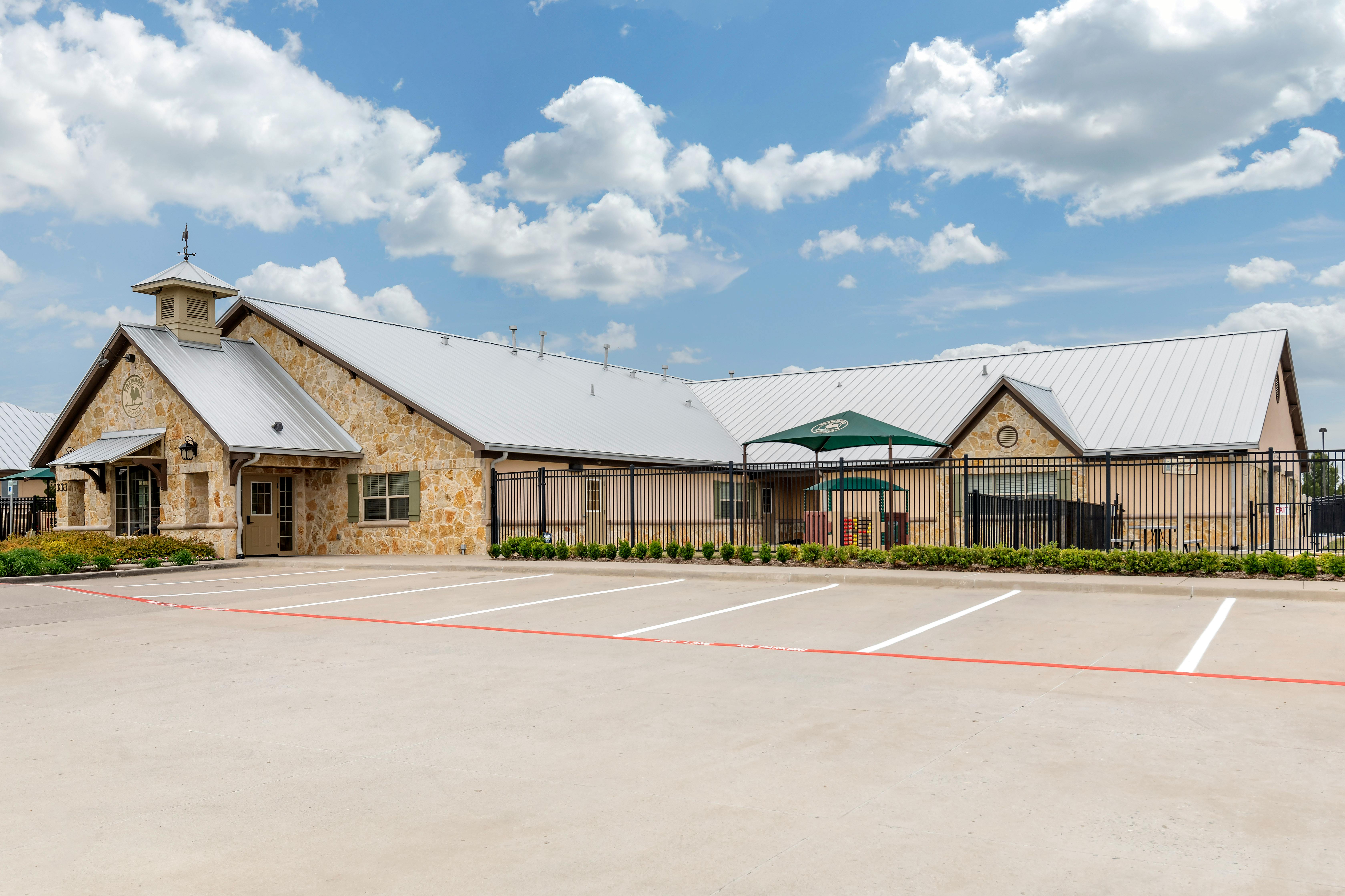 Exterior view of a stone building with a parking lot and a playground under a green canopy
