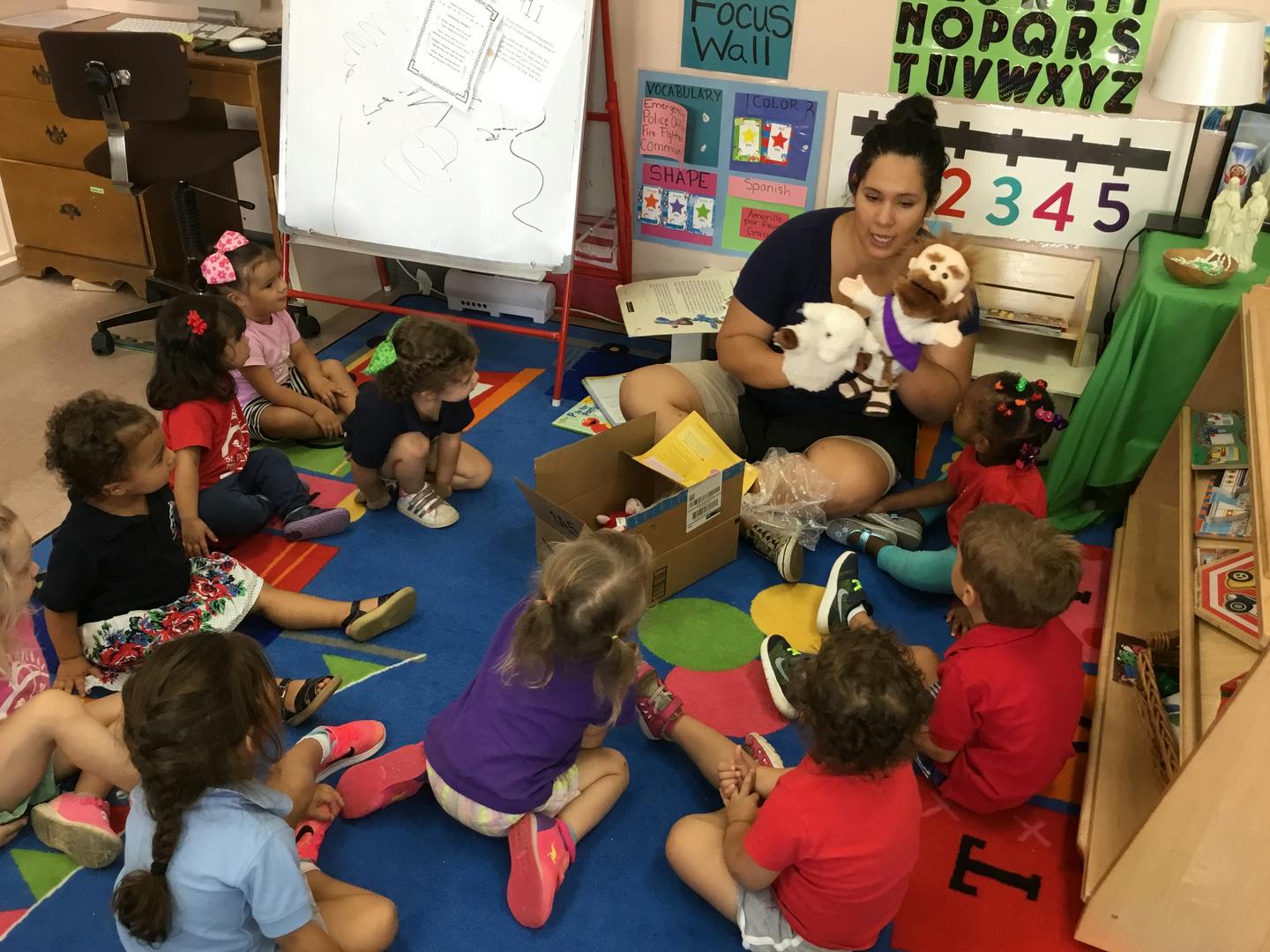 Adult and children sitting on a rug, adult holding puppets