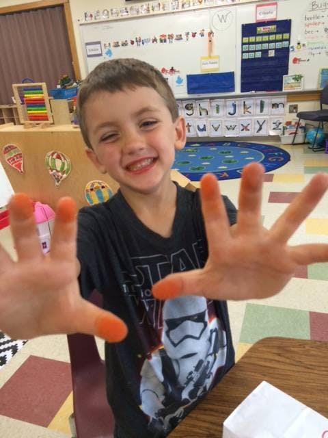 Child with orange-stained fingers in a classroom