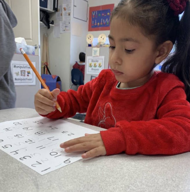 Child in red shirt writing on a paper with numbers