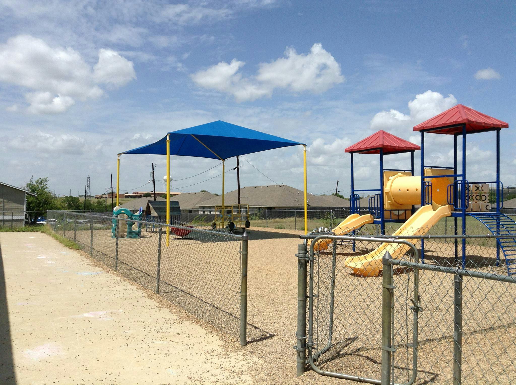 Playground with slides, swings, and a blue shade structure under a blue sky