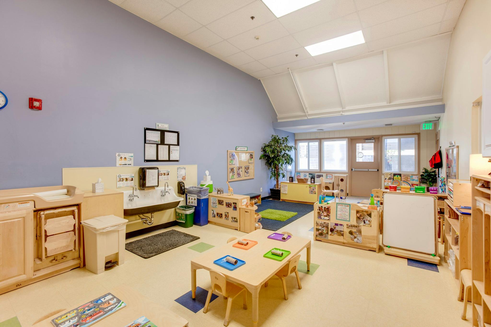 Empty classroom with small tables and chairs, sinks, and shelves