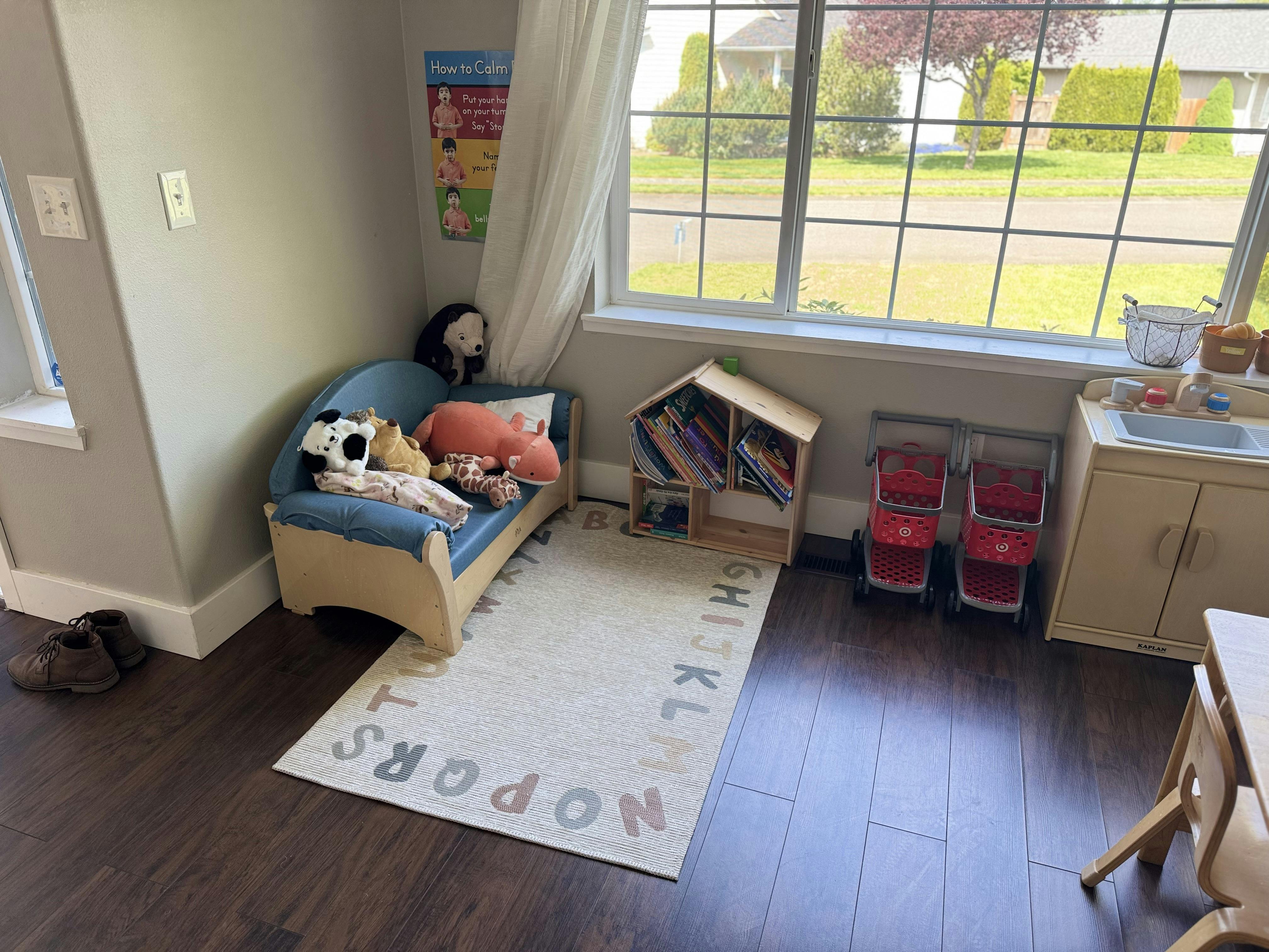 Child's play area with a small sofa, bookshelves, play kitchen, and alphabet rug