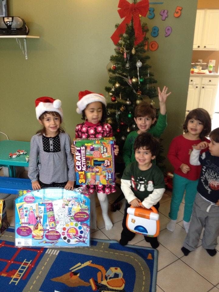 Children in Santa hats holding gifts in front of a Christmas tree